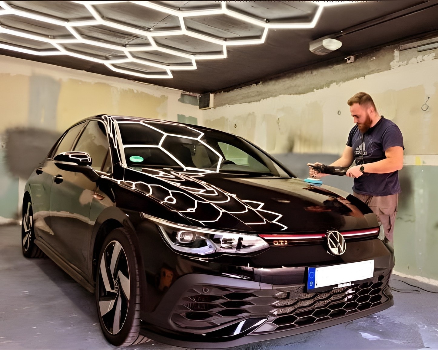 Detailer machine polishing the hood of a black Volkswagen Golf GTI under LED lighting in the Selmo Garage workshop in Sarajevo